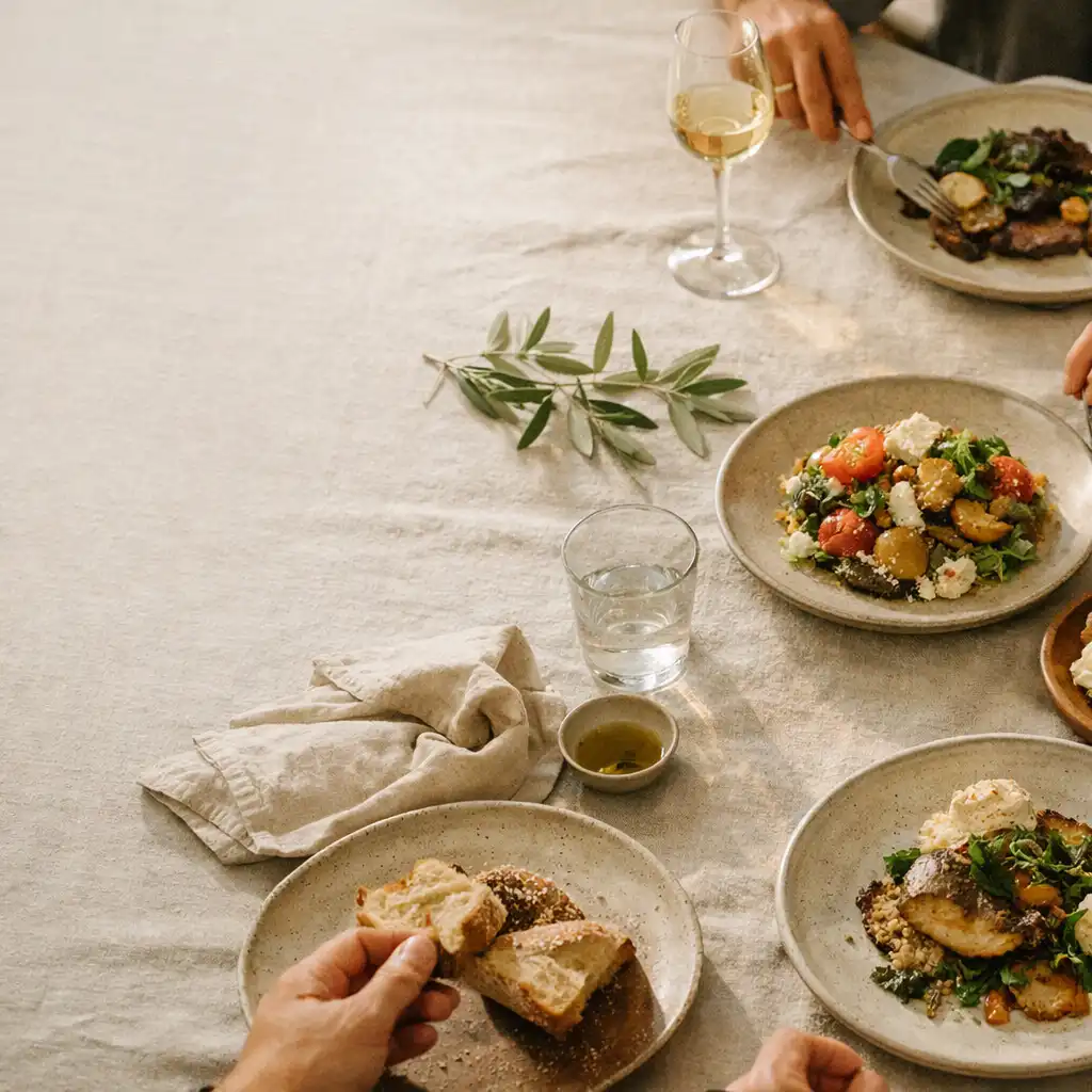 Wspólny restauracyjny stół z ceramiką, lnianą serwetą i dłońmi gości